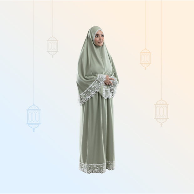 Woman wearing an olive green prayer outfit with intricate lace trim on sleeves and hem, standing in front of a soft gradient background.