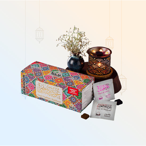 Decorative incense set featuring a colorful patterned box and small packets of bukhour with a lit bronze burner and dried flowers.